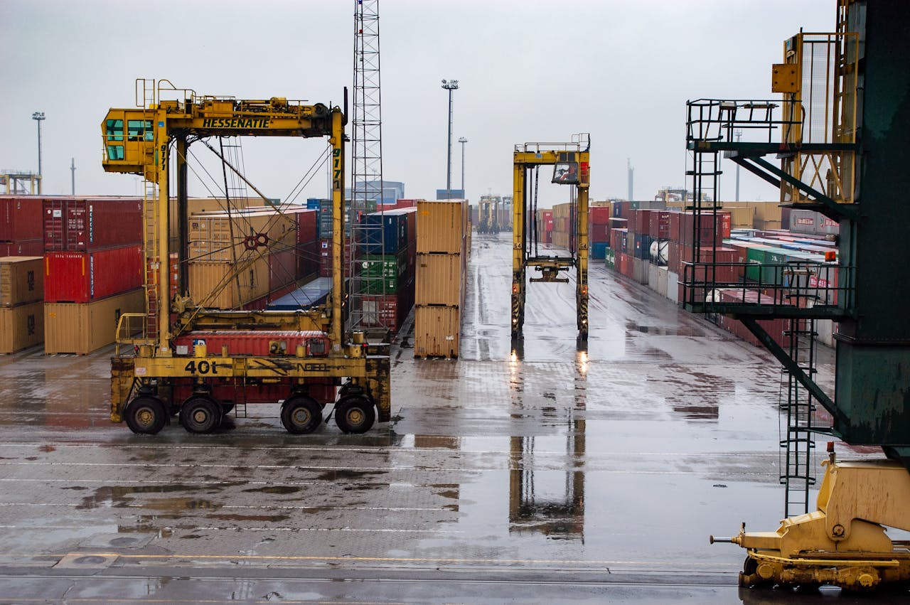 Container yard featuring straddle carriers and stacked containers under a rainy sky.
